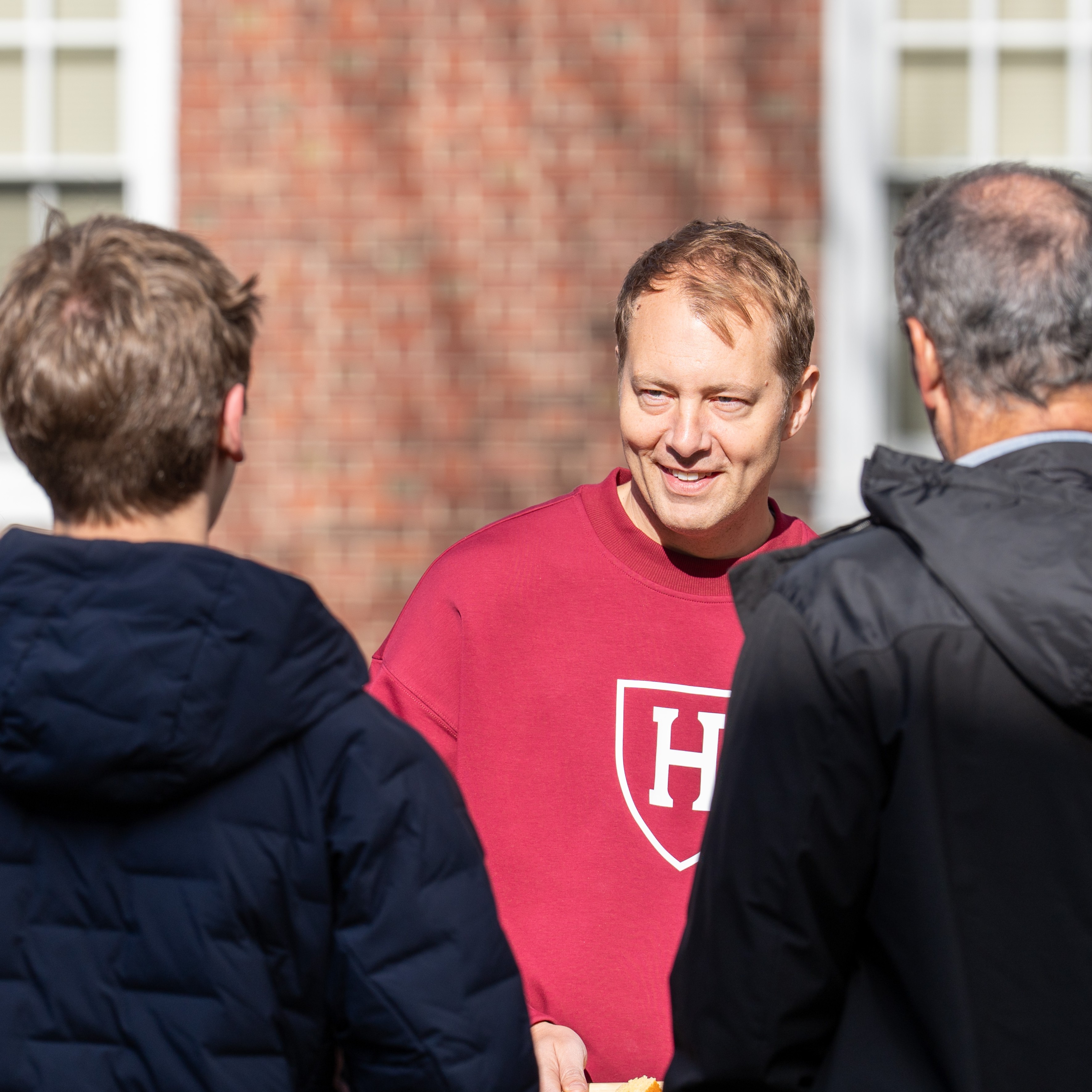 Dean Deming, dressed in a crimson Harvard Athletics sweatshirt, speaks with families of Harvard students at the Family Weekend block party.
