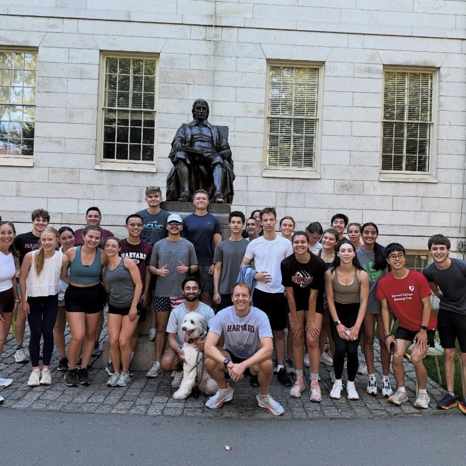 Dean Deming and members of the Harvard Running Club pose for a group photo by the John Harvard Statue in Harvard Yard after a morning run.