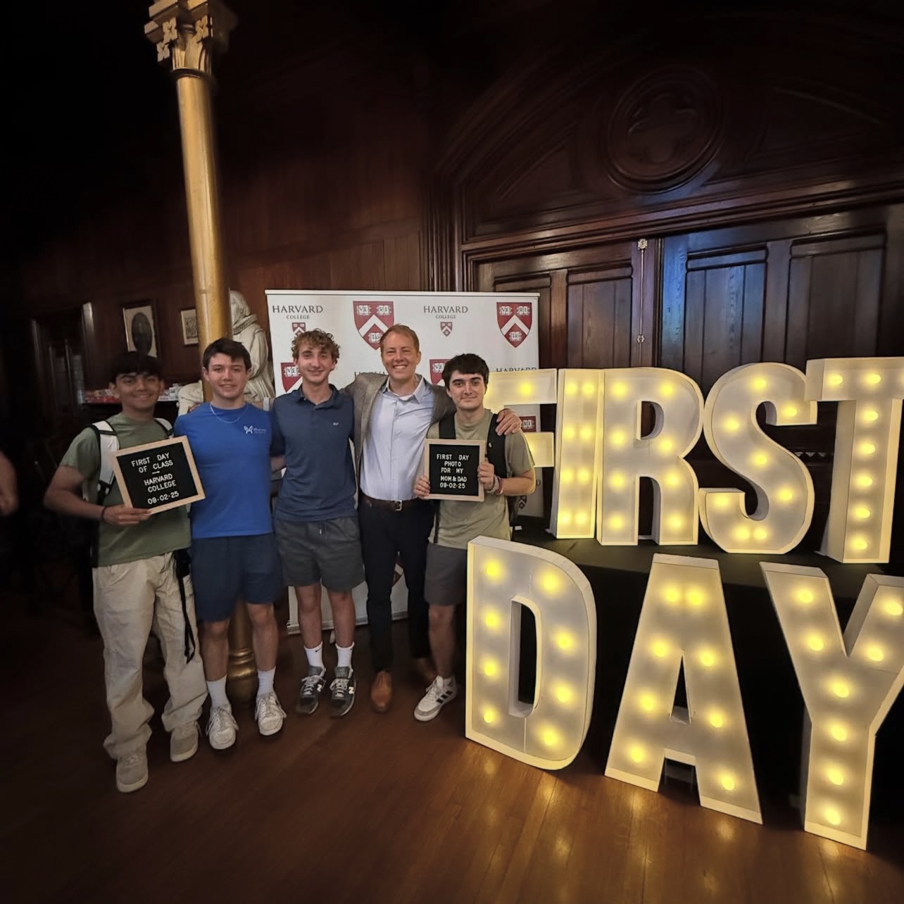 Dean Deming and four first-year students pose for a group photo by the “First Day” light sign in Annenberg Hall.